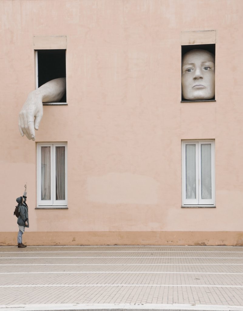 Some art work on a street where one window has a face and the other has a hand coming out