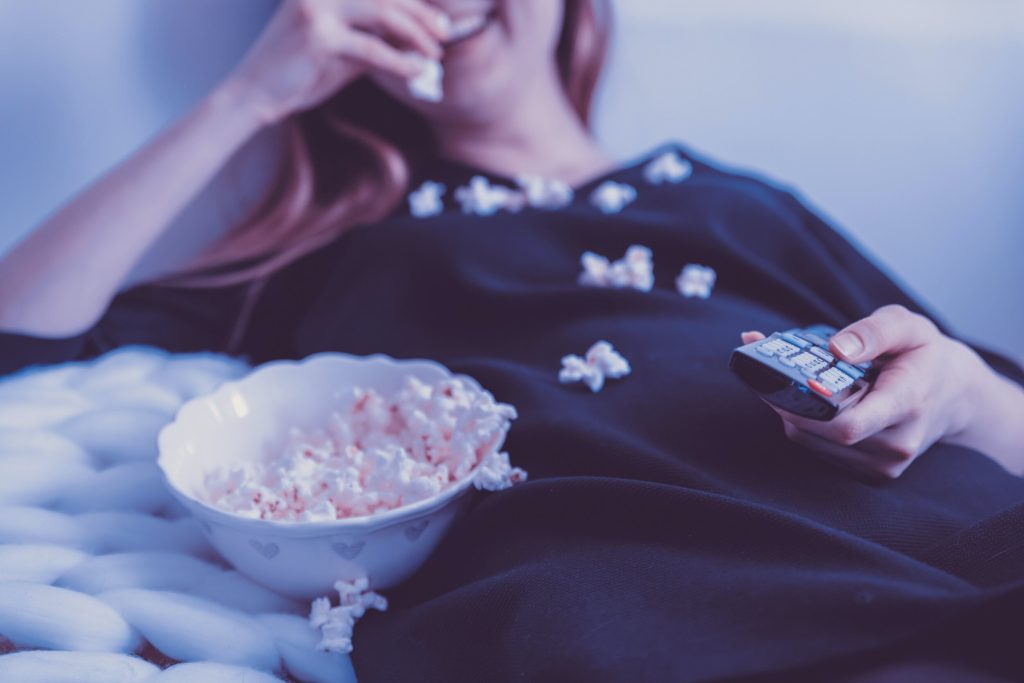 Someone smiling and eating popcorn while holding a television remote