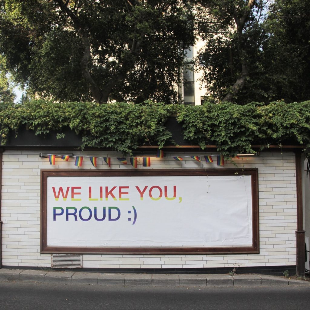 A photograph of a billboard that reads "We like you, proud" and a smiley face emoticon