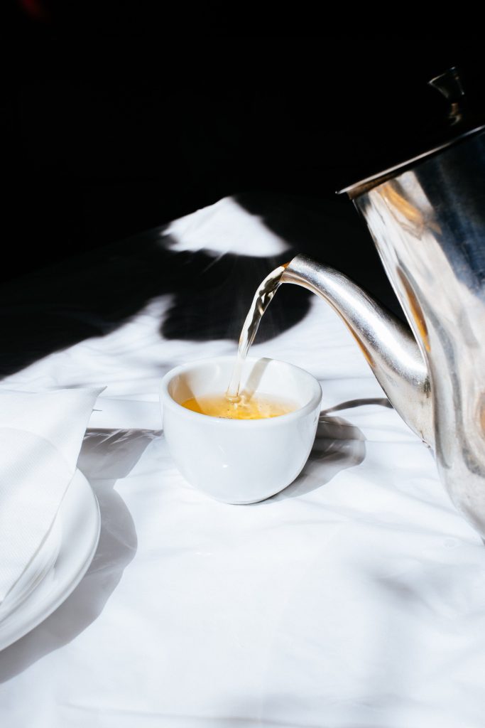 A photograph of tea being poured into a cup from a metal teapot