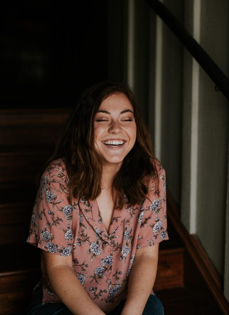 A female sitting on a staircase laughing, with her eyes closed