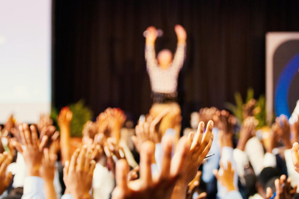A crowd at a seated event, with people with their hands in the air