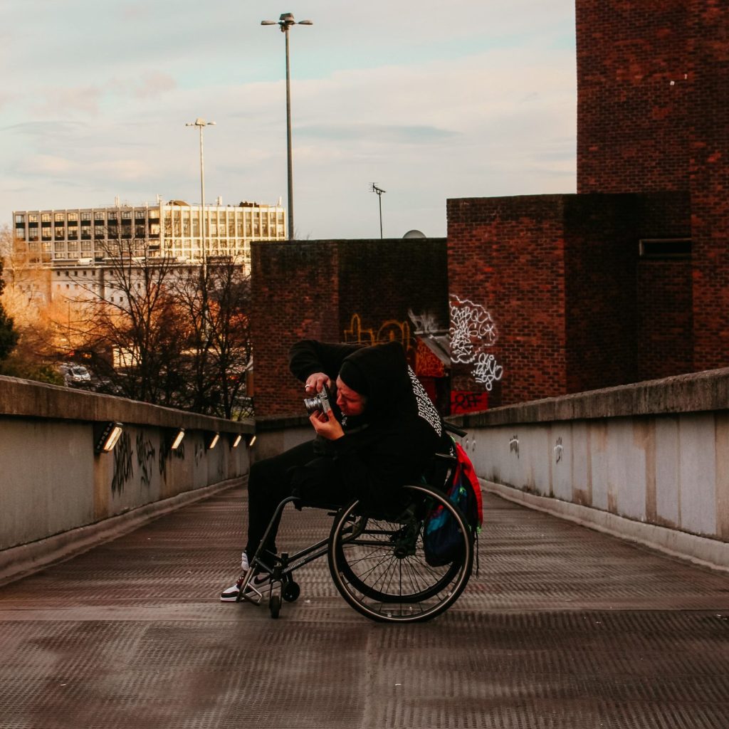 A person in a wheelchair taking a photograph with a film camera