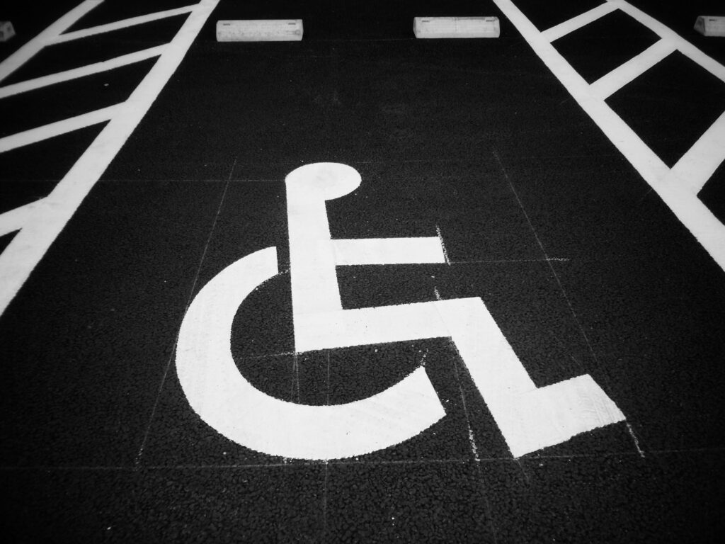 A white wheelchair symbol contrasting against the black tarmac of a parking space